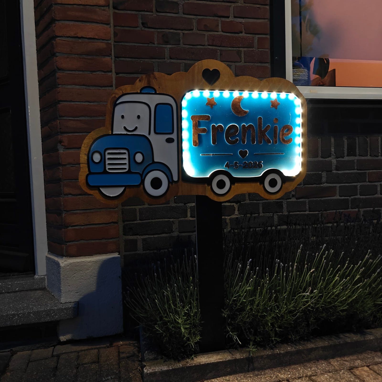Verlicht geboortebord in de vorm van een vrachtwagen met de naam Frenkie, buiten op een paal
