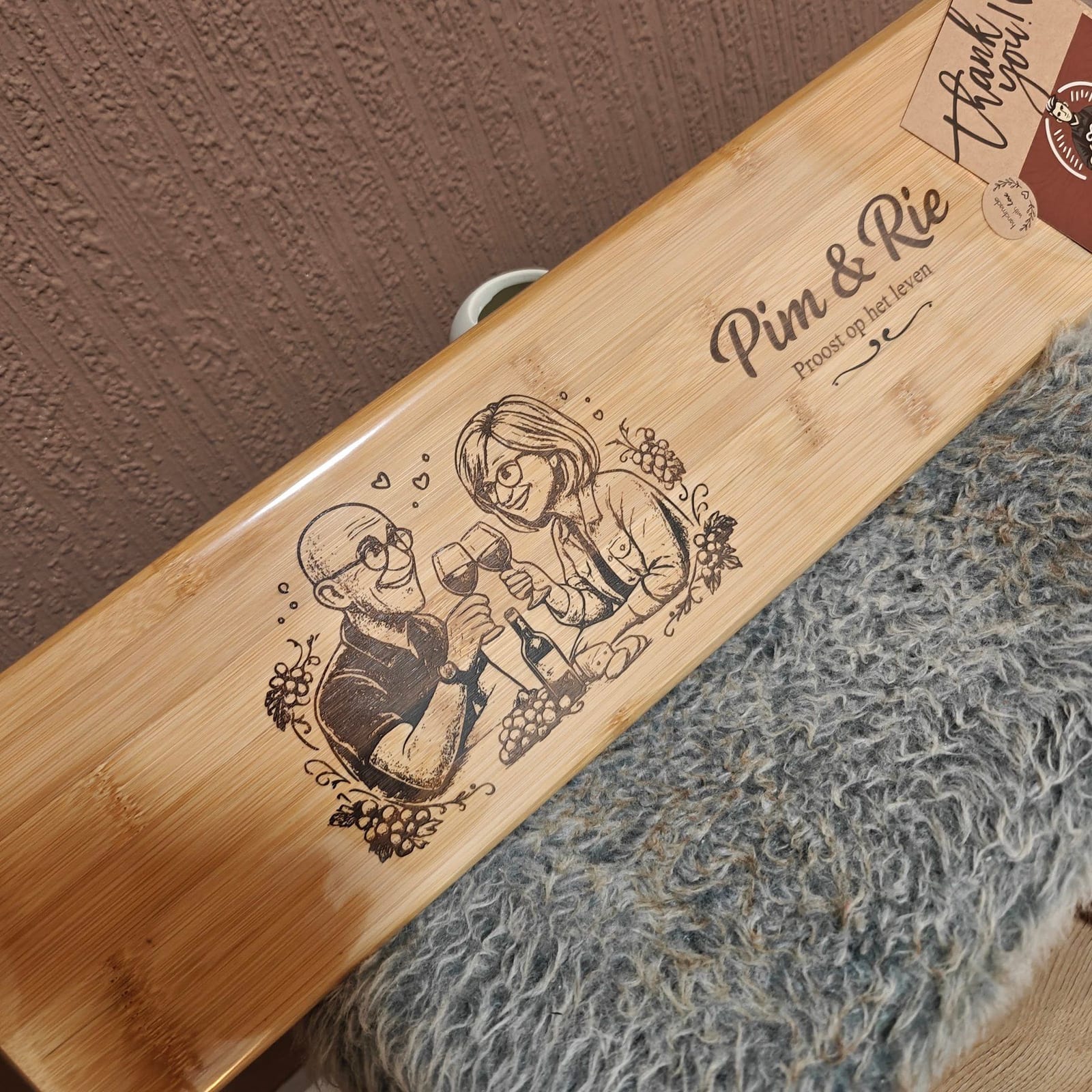Bamboe plank met een gegraveerde cartoon van een proostend echtpaar en hun namen