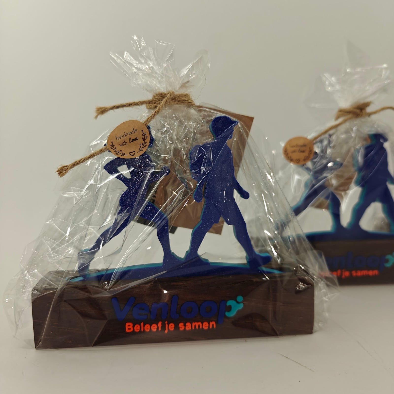 Ingepakte sponsorgeschenken voor de Venloop: een wandelaar en een hardloper in blauw op een houten voet met het logo van het evenement