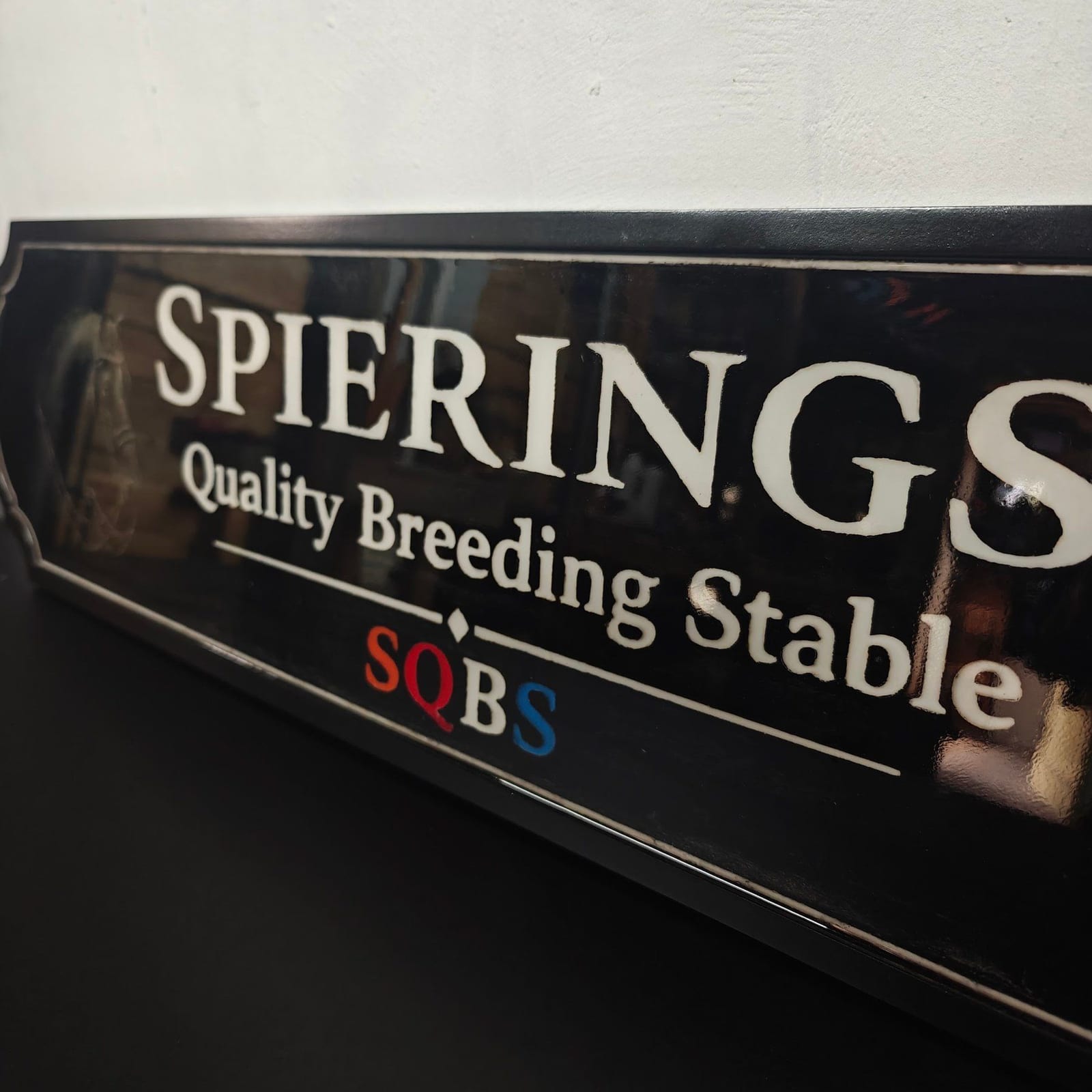Zwart naambord van fokstal Spierings Quality Breeding Stable met witte letters en een gegraveerd paardenportret