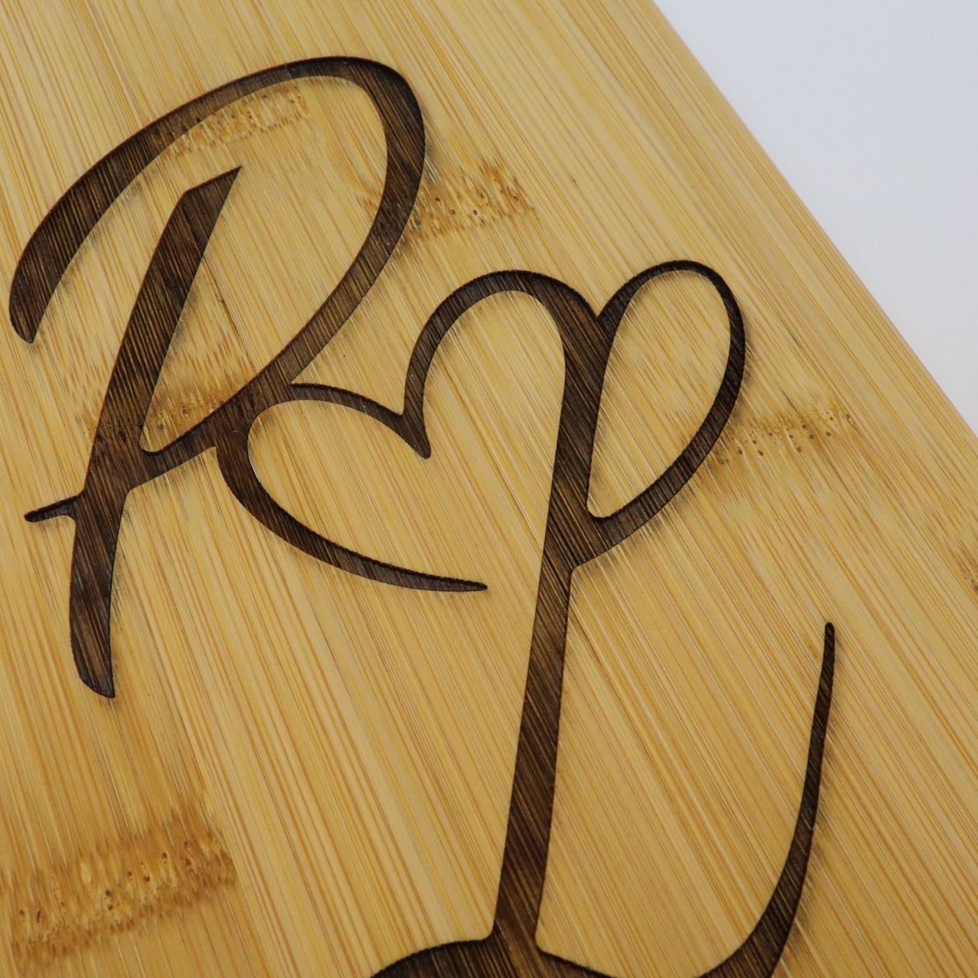 Detailopname van een gegraveerd monogram in bamboe, waarop de diepte van de gravure en de nerf te zien zijn