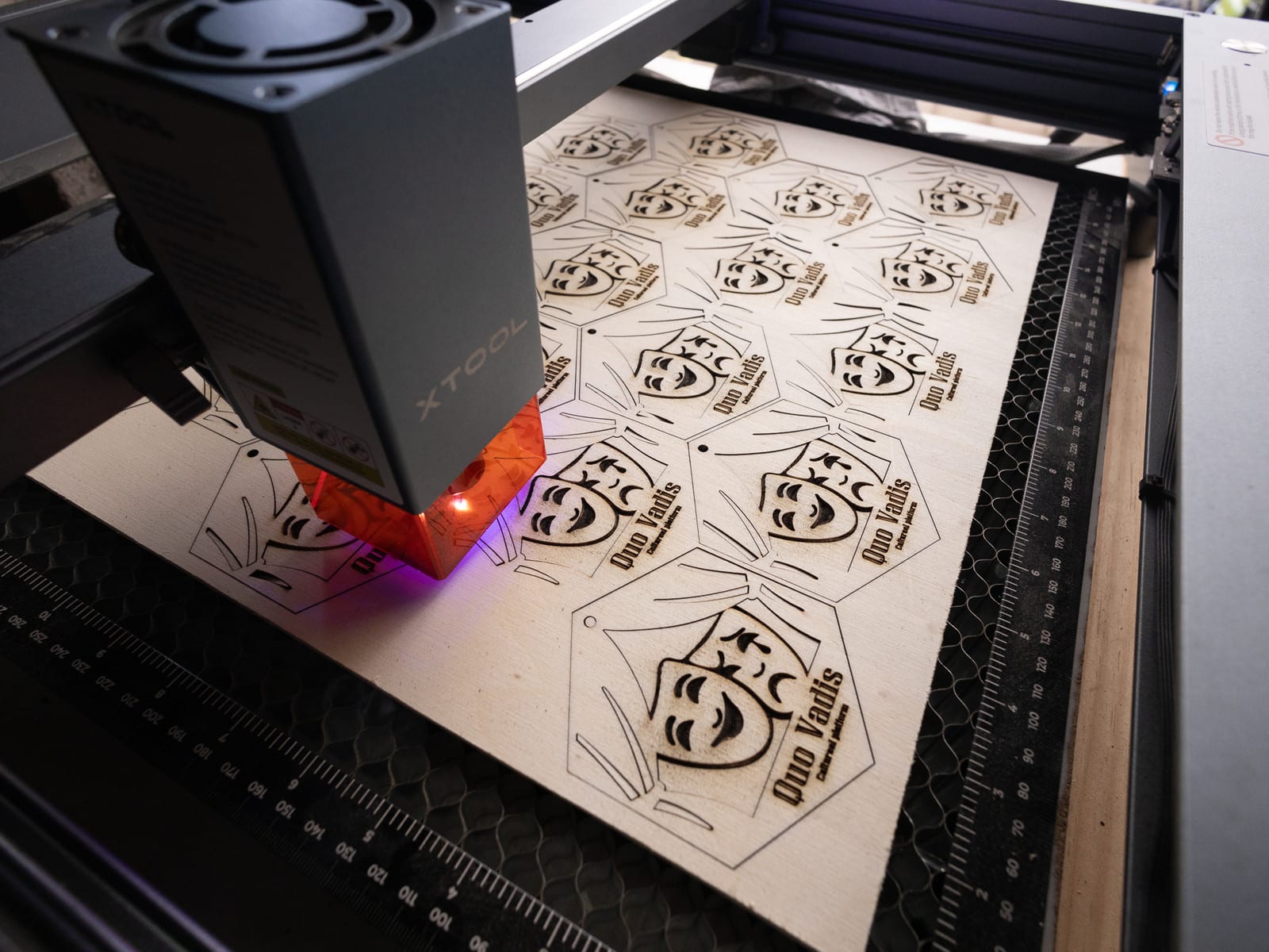 De laser snijdt een plaat vol houten labels met hetzelfde logo, voor een serie kerstgeschenken