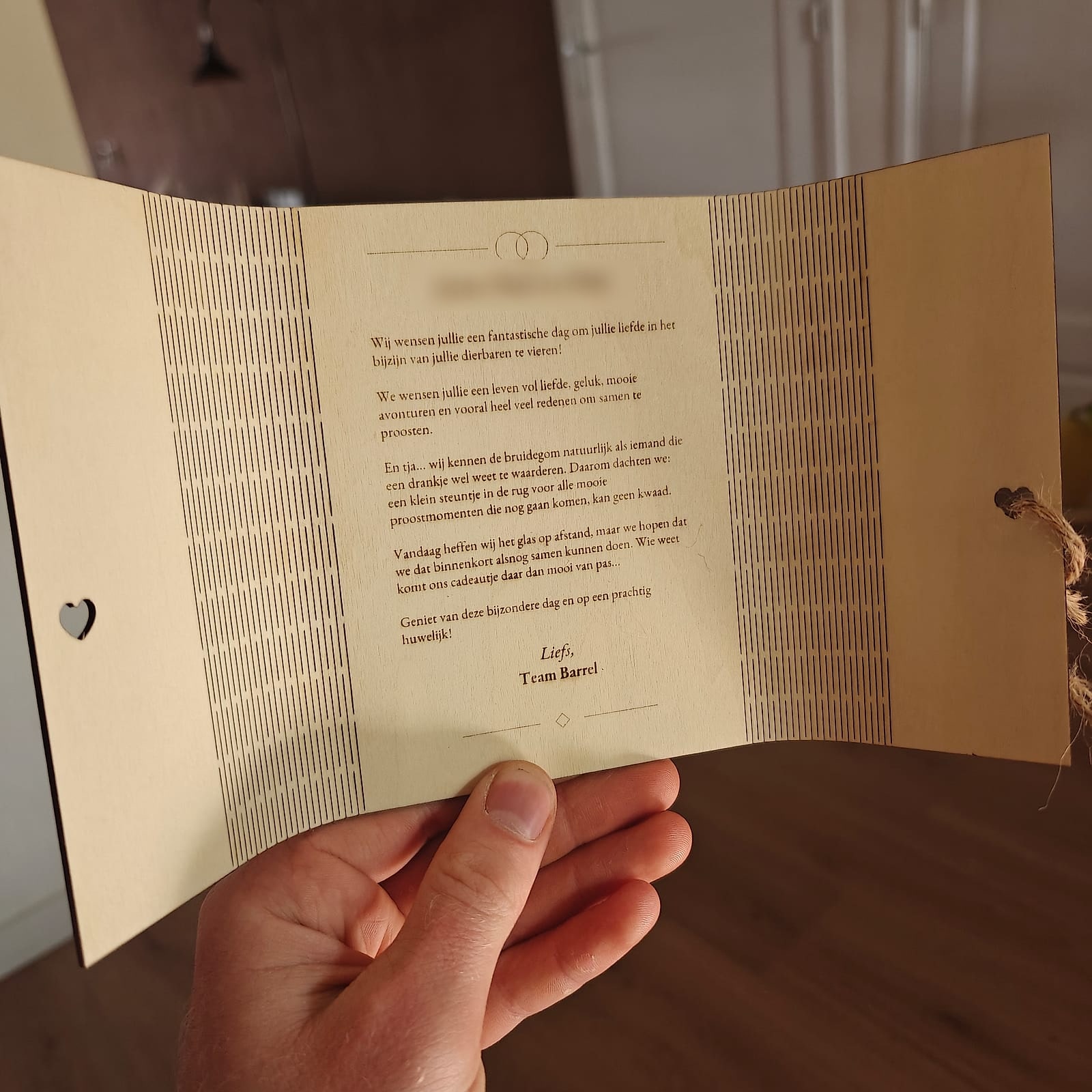 Lasergesneden houten trouwkaart, opengeklapt, met een gegraveerde brief en een touwtje met hartje