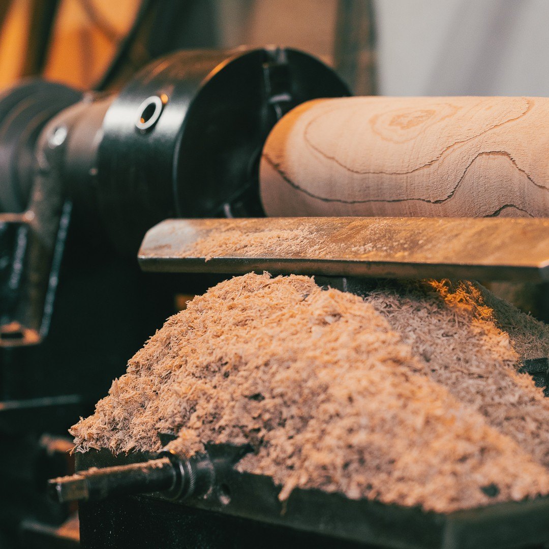 Een blok hout in de draaibank, met een berg verse houtkrullen op de leunspaan