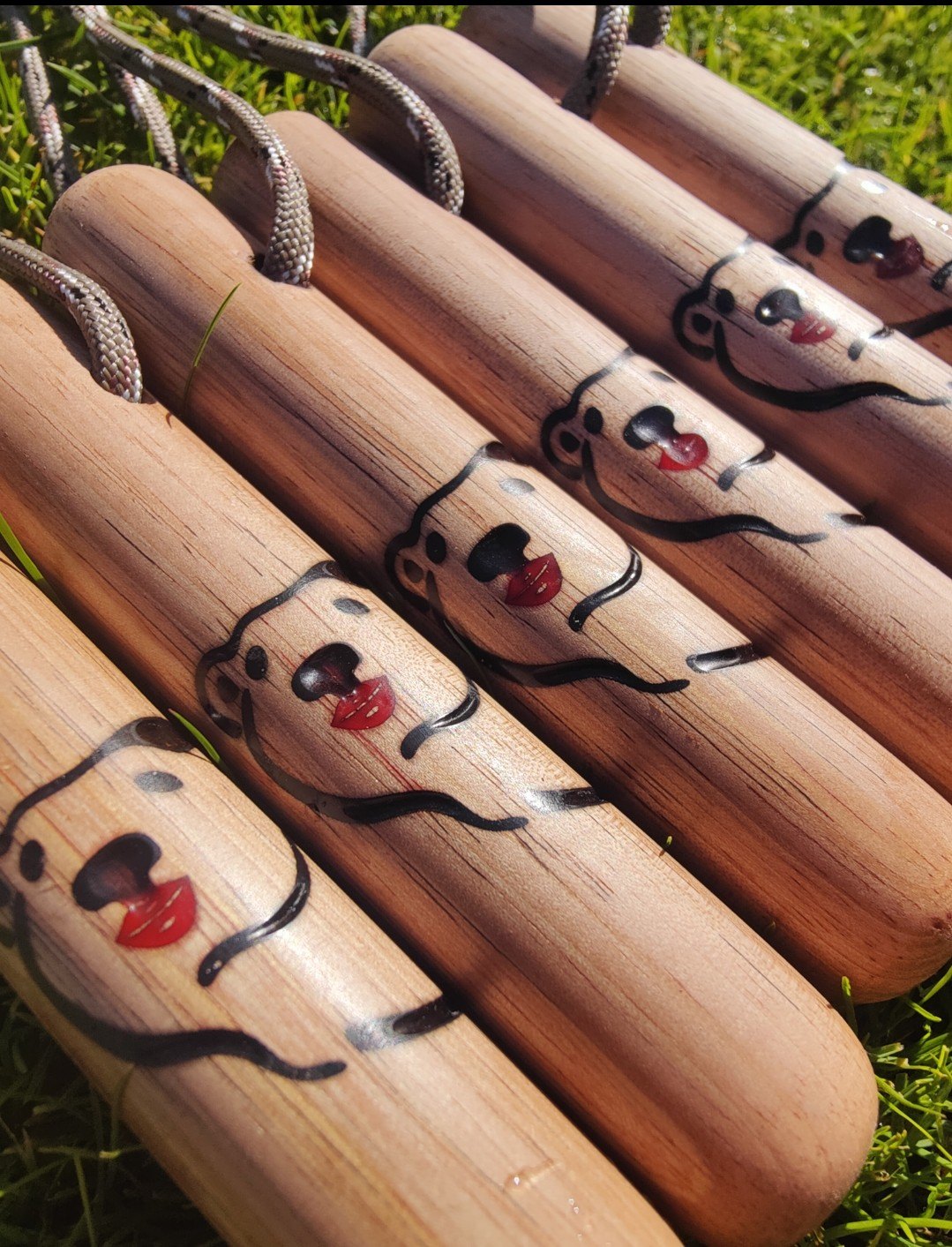 Rij houten wandelstokjes met een koord en een gegraveerd beertje met rode lippen, op het gras